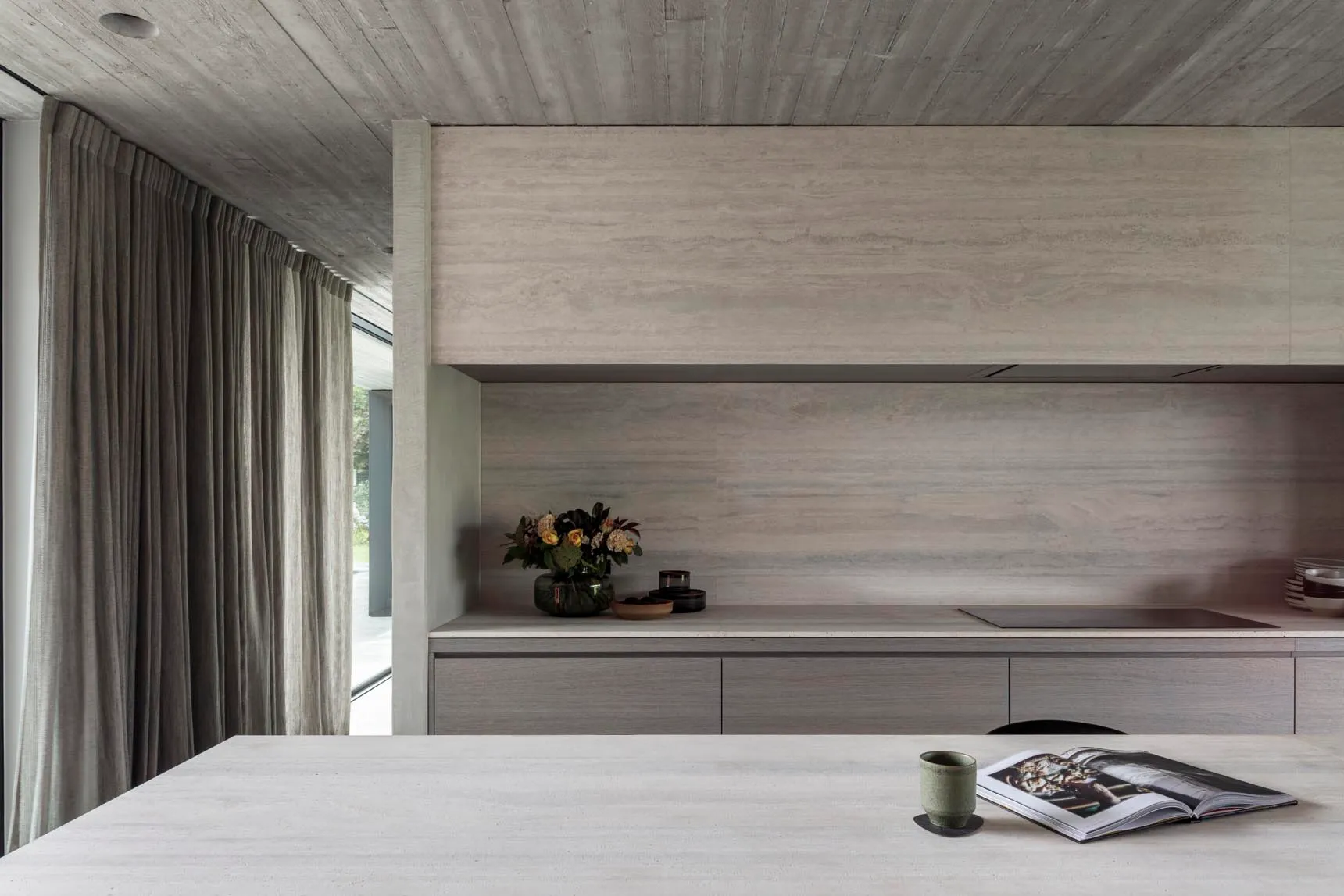 A modern, minimalist kitchen with concrete countertops and a large window.