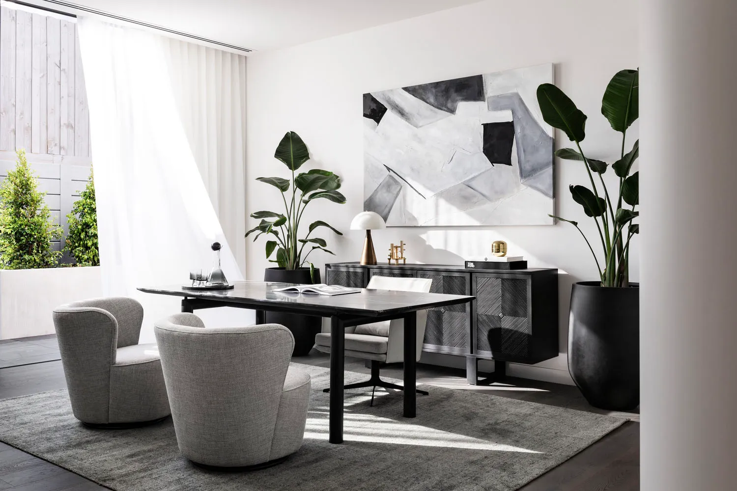 A modern home office with a sleek, black desk, grey upholstered chairs, and a large abstract painting on the wall.