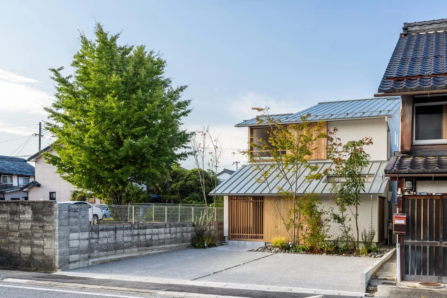 Modern residential exterior featuring a metal roof, wooden frames, and a concrete driveway surrounded by greenery.