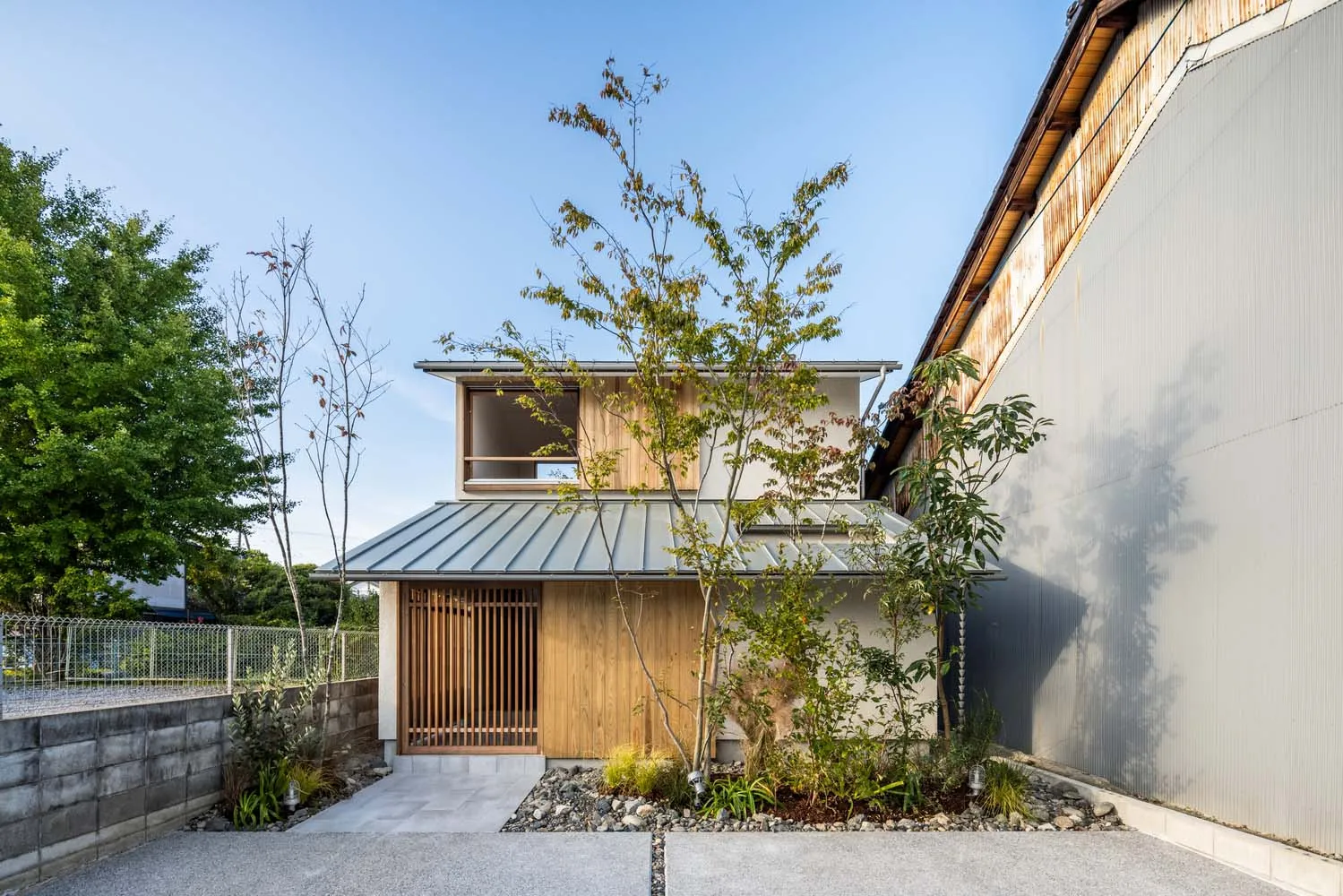 A modern residential exterior with a metal roof and wooden structure, featuring a minimalist design and a small garden with t