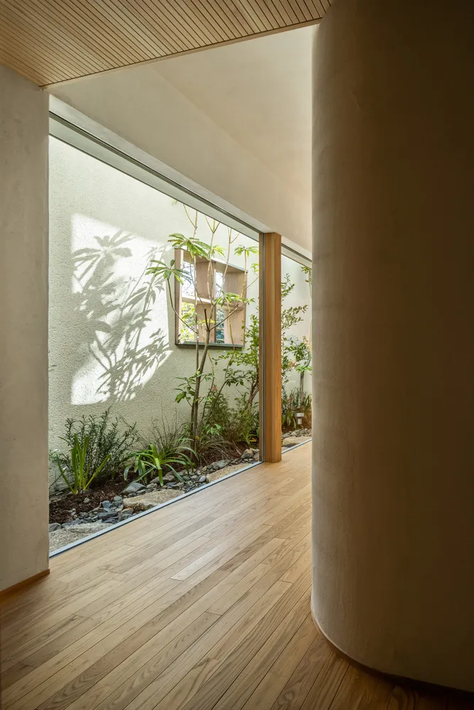 A minimalist entryway features a concrete and wooden floor with a small garden area next to it.