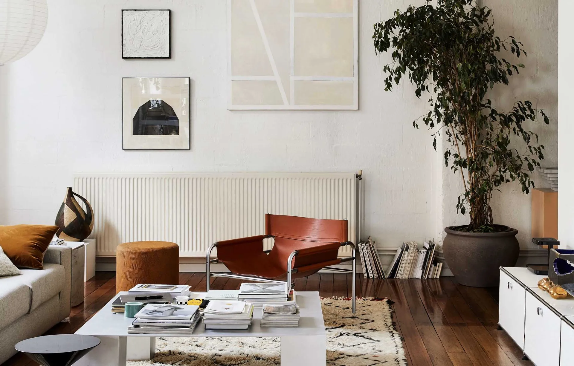 A modern minimalist living room featuring wood flooring, indoor plants in a clay pot, and leather furniture.