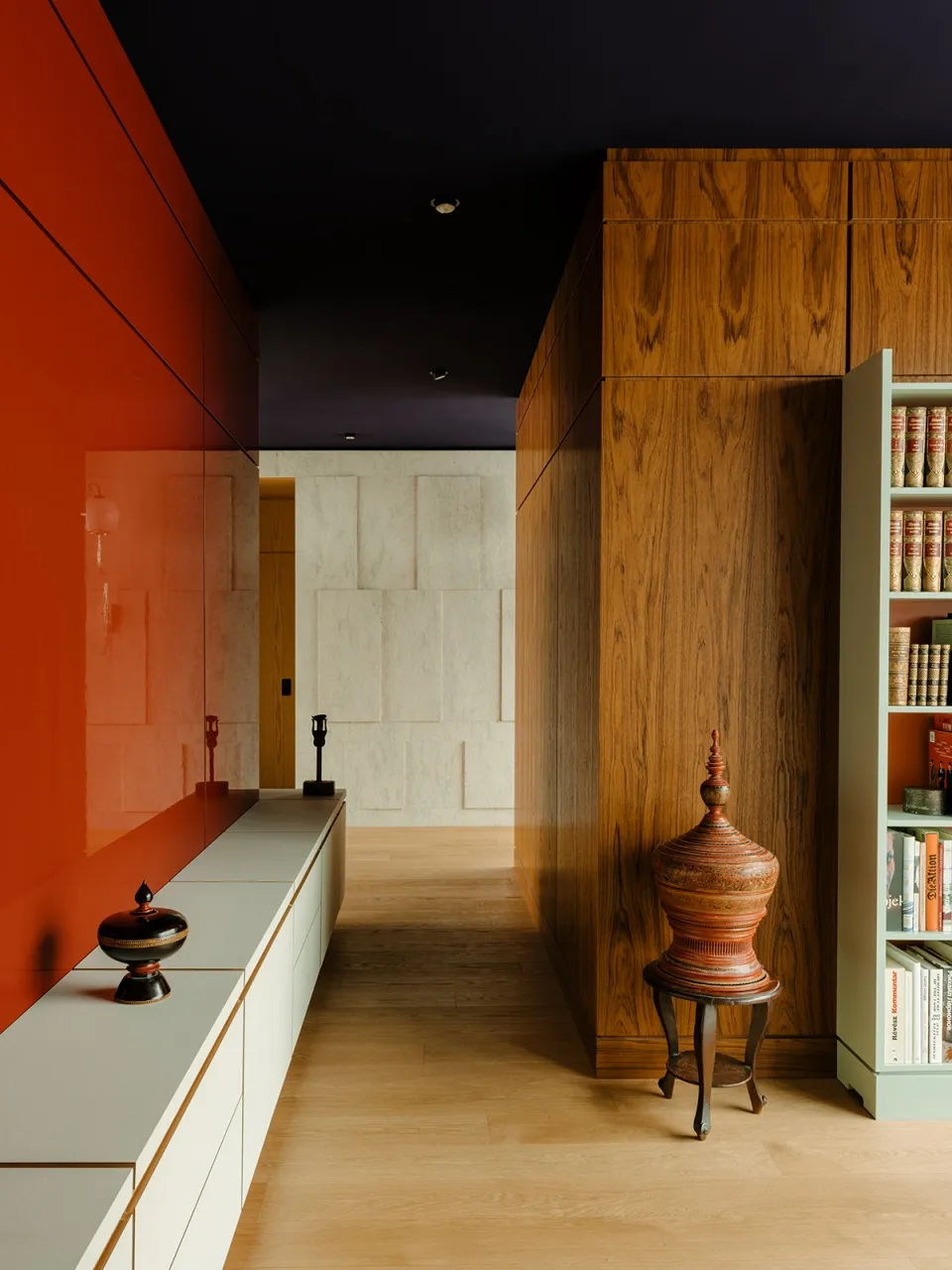 A modern hallway featuring a red wall, wooden cabinets, and a bookshelf with books.