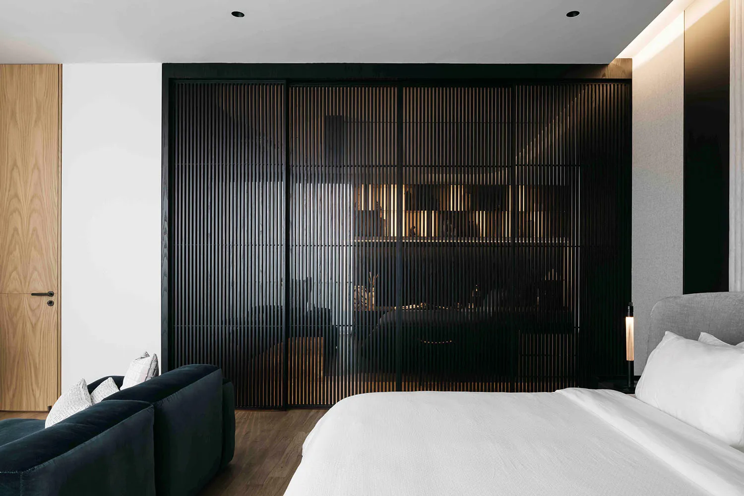 A modern minimalist bedroom featuring a metal wall, a bed with white sheets and gray headboard, and a large sofa with white p