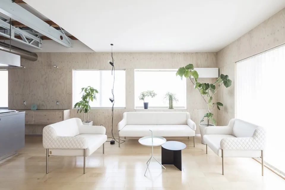 Minimalist living room with white furniture, green plants, and wooden walls and flooring.