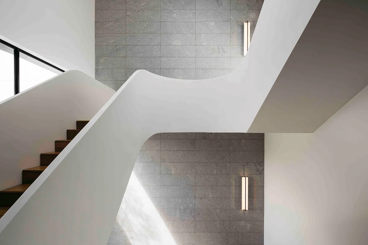 A modern concrete staircase with a wavy design, adorned with natural leaves scattered along the steps and landing.