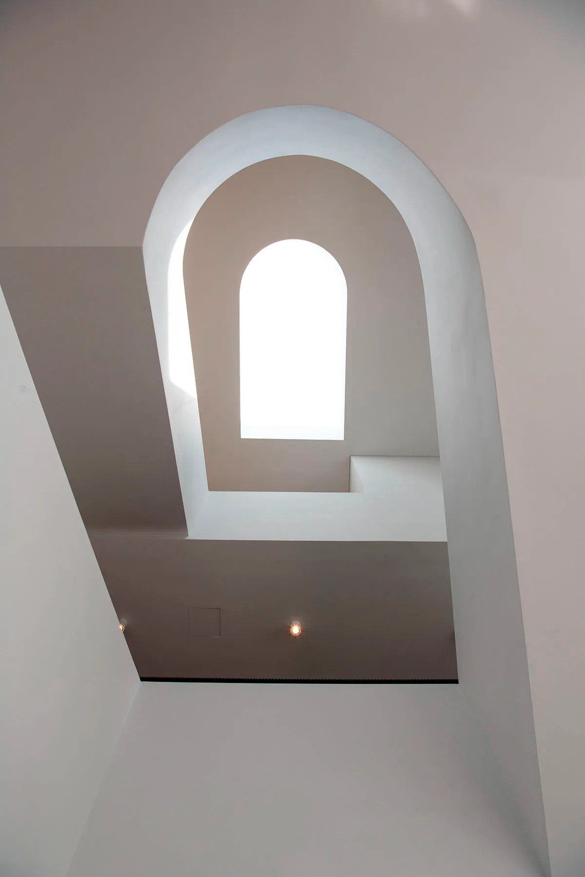 White arch-shaped stairwell with a bright window at the center.