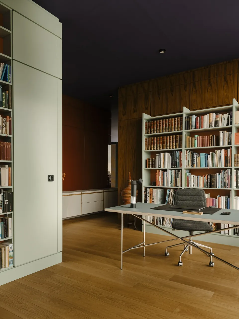 An image of a minimalist office space with modern materials, featuring a desk, bookshelves, and a chair.