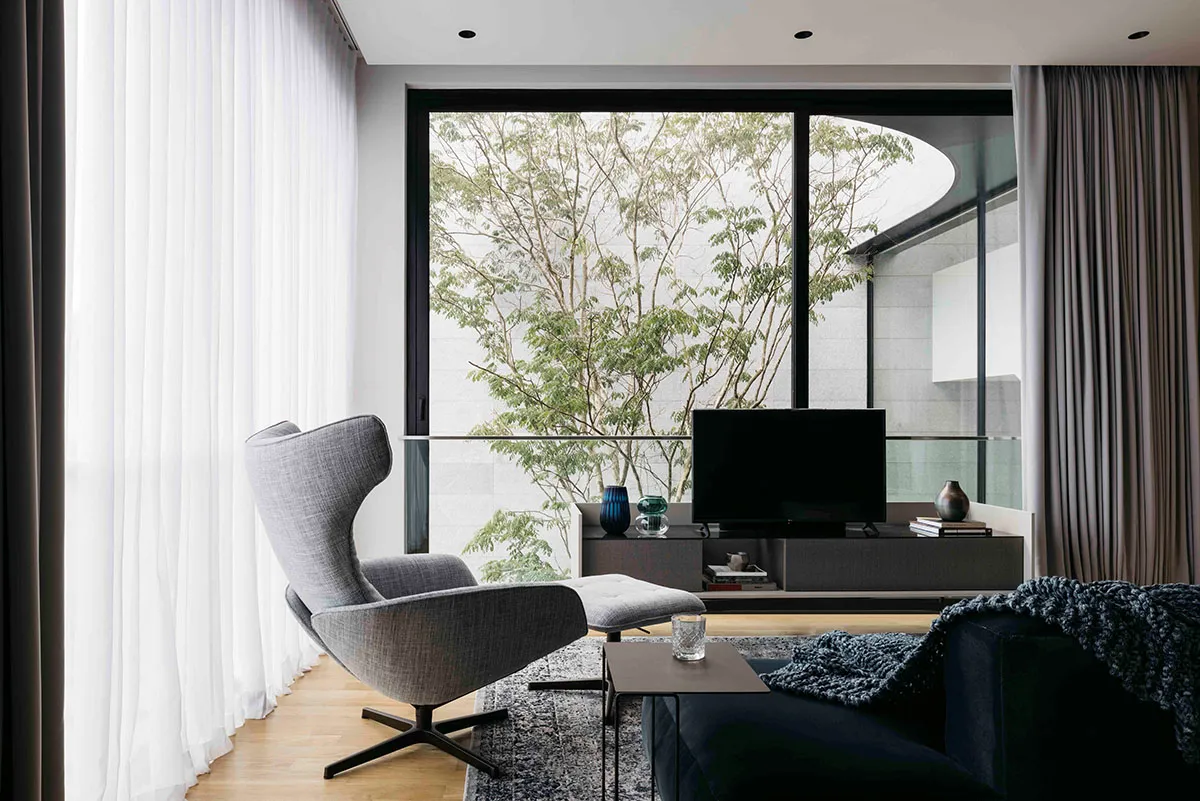 A modern minimalist living room featuring gray fabric furniture, a large glass window, and a glass coffee table.