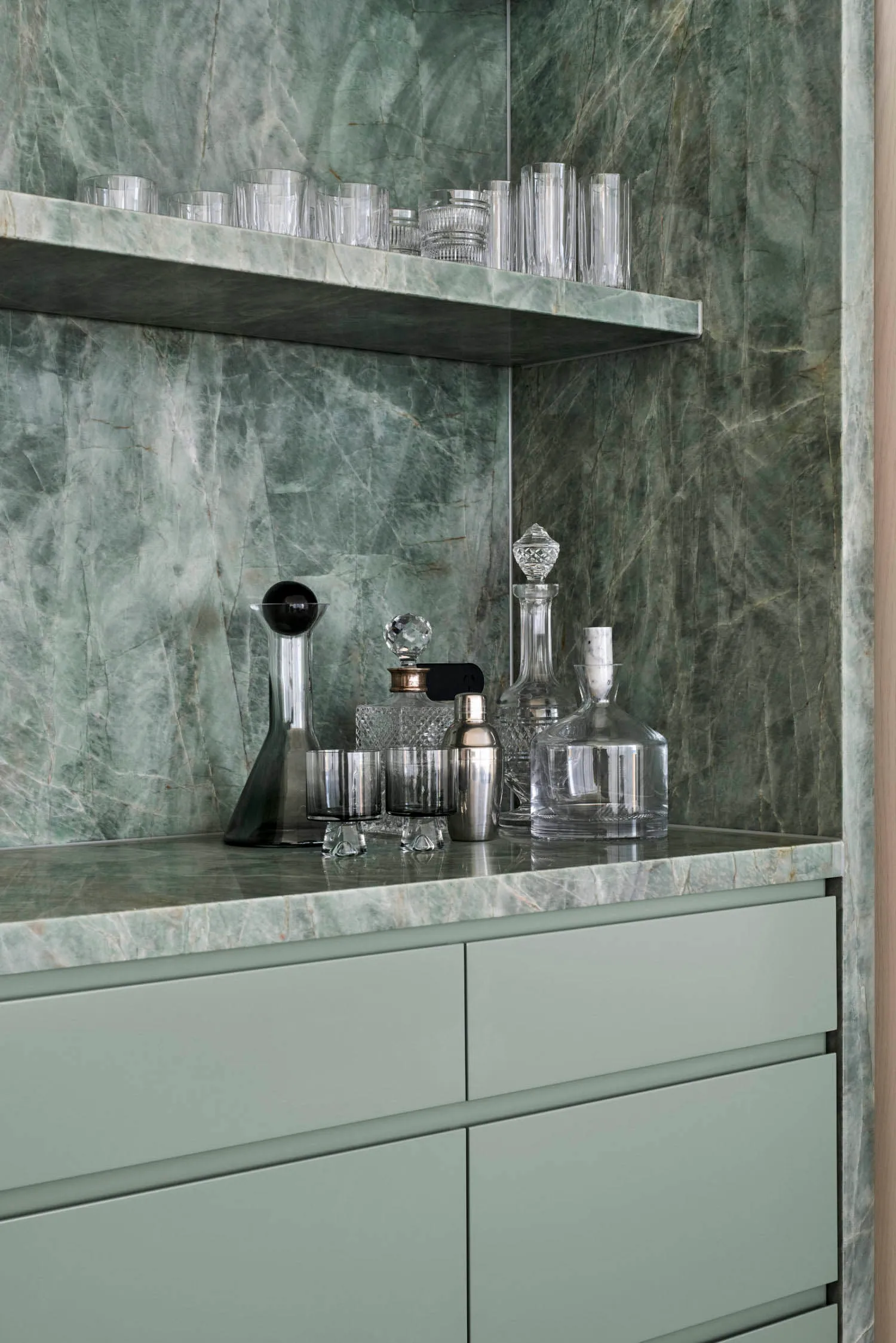 A modern bar counter featuring marble materials, with various glassware and decanters on a countertop.