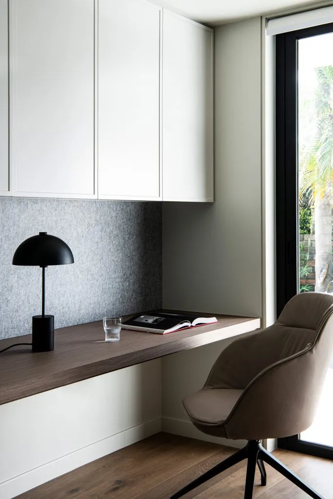 Minimalist office space featuring wooden desk, fabric chair, and metal lamp.