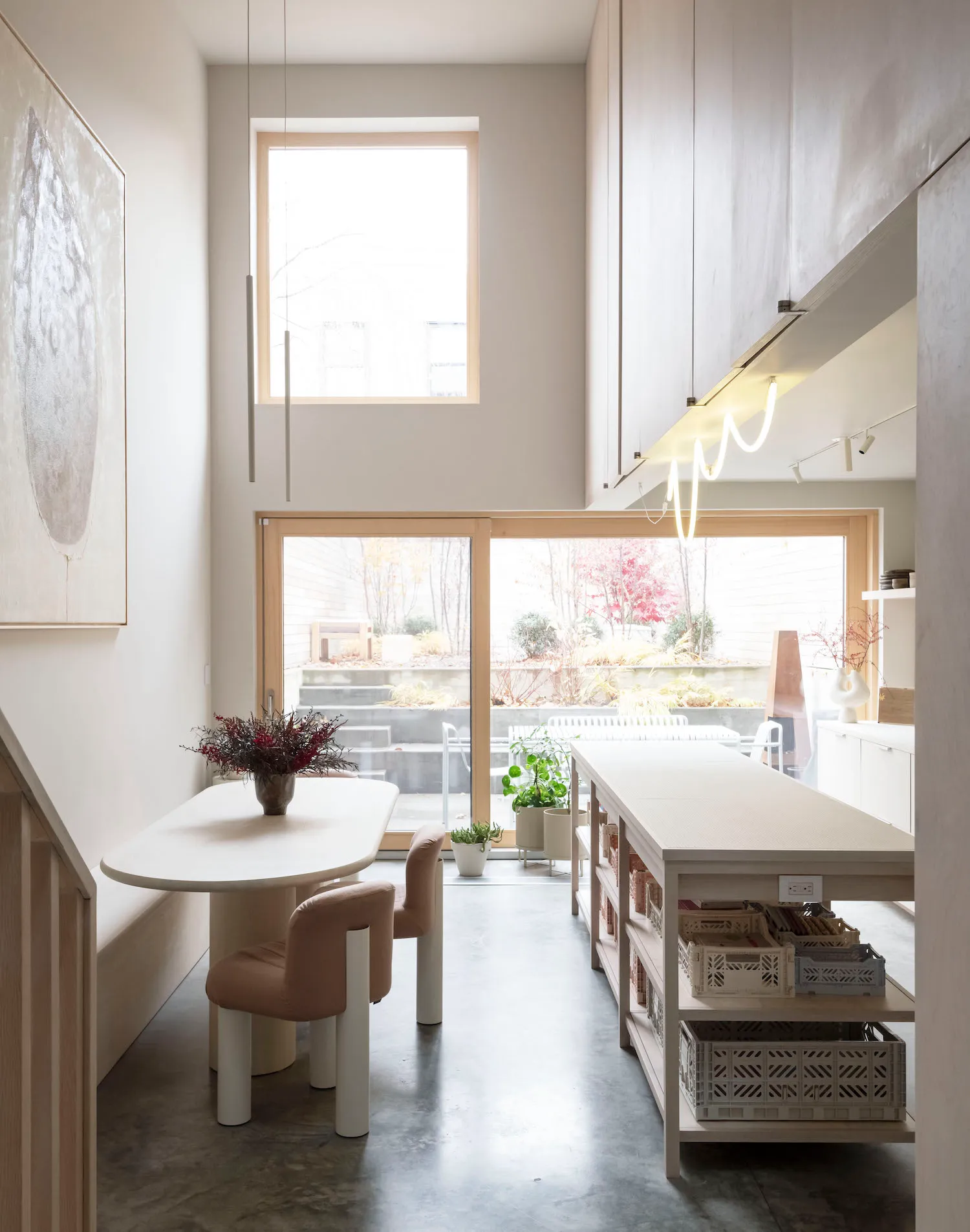 A minimalist residential kitchen with concrete flooring, a white dining table, and a large window.