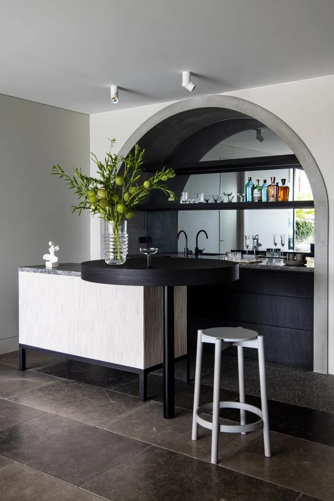 A modern bar counter made of concrete with a vase of greenery and a stool.