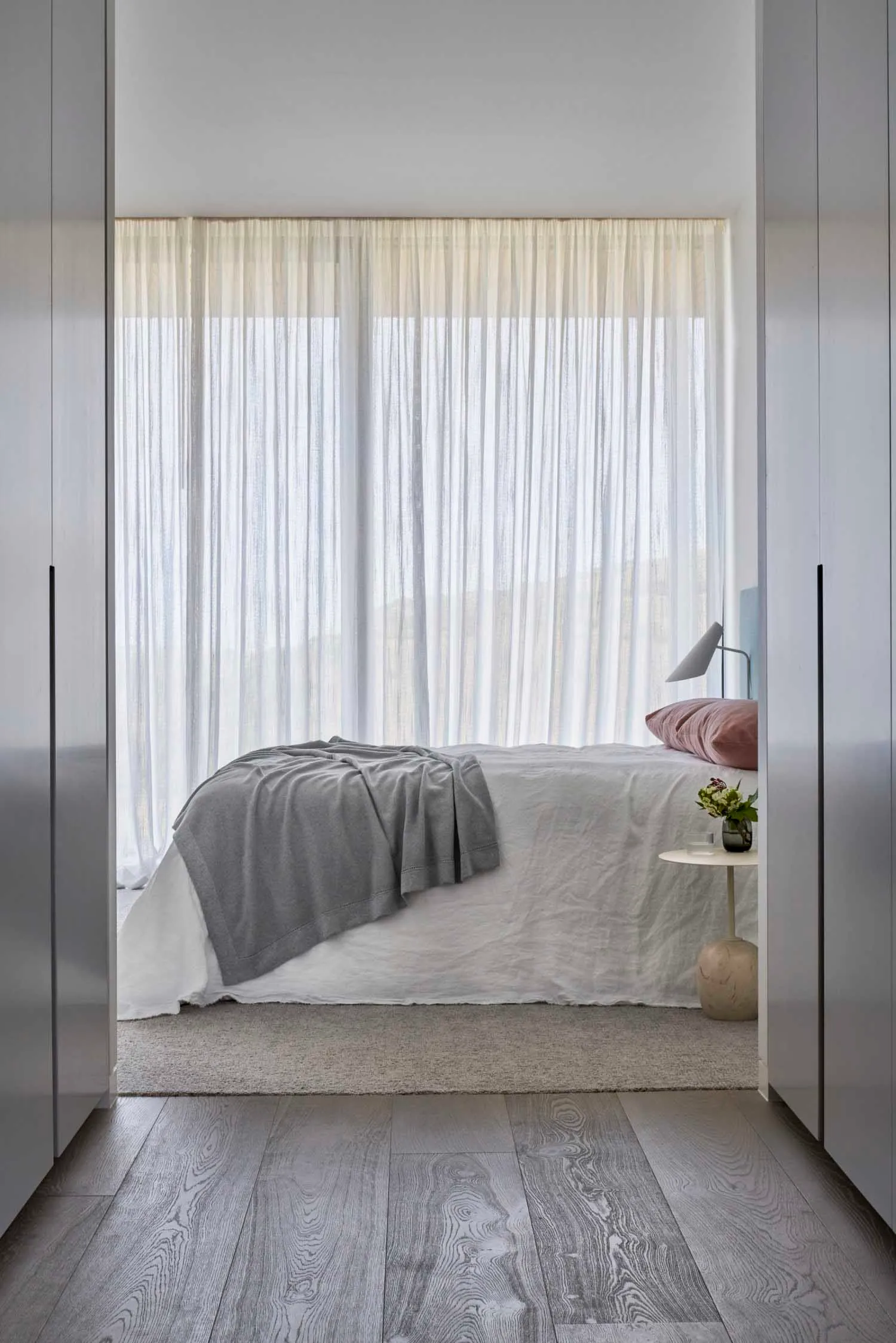 A modern minimalist bedroom with a bed, curtains, and a side table.