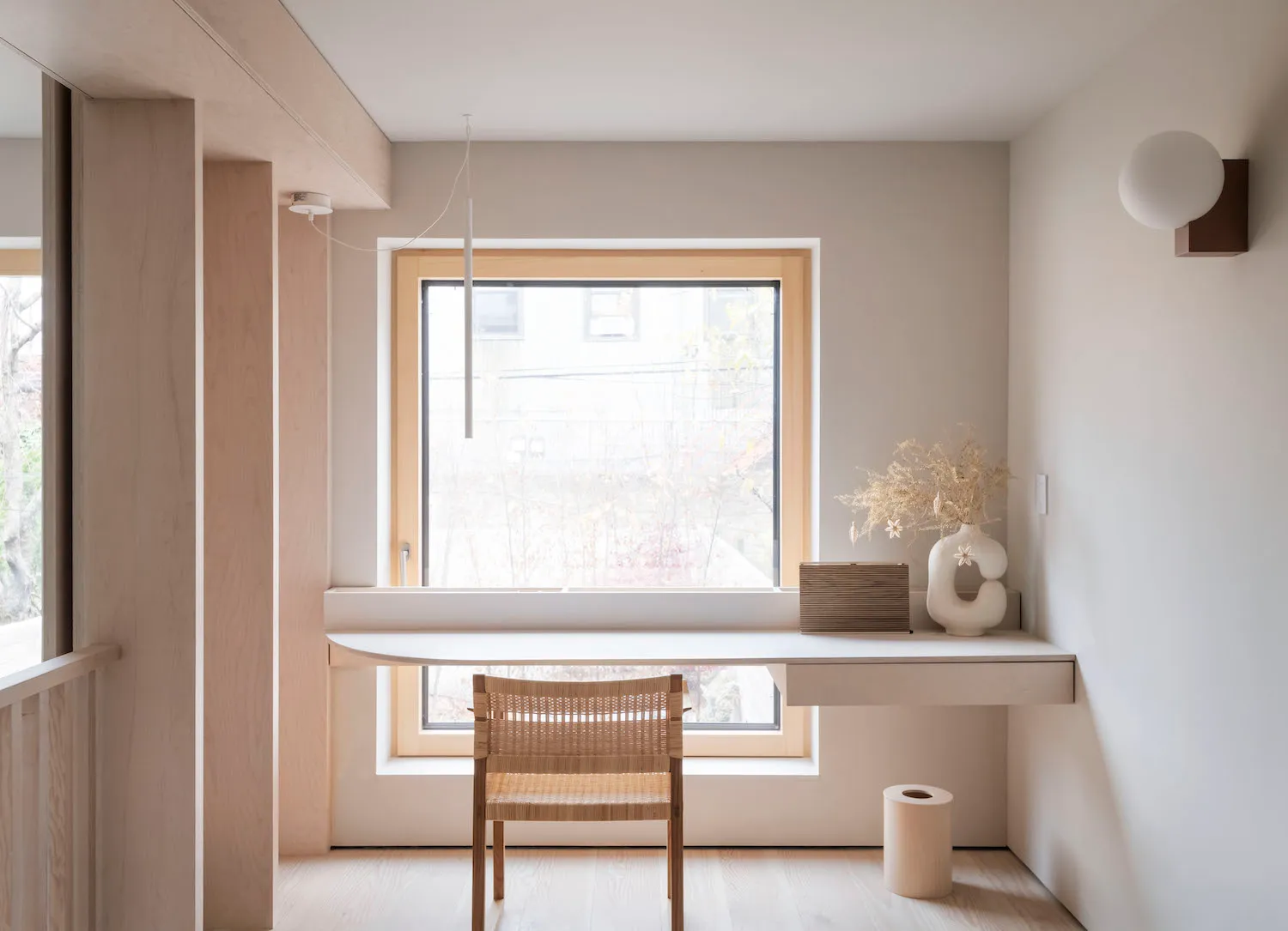 A minimalist home office with a small white desk, wooden chair, and a vase of flowers.