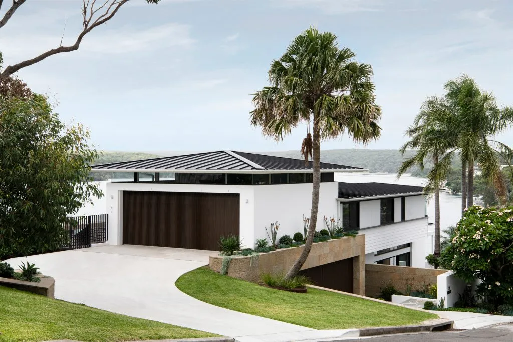 A modern house with a concrete exterior, featuring a large driveway and palm trees.