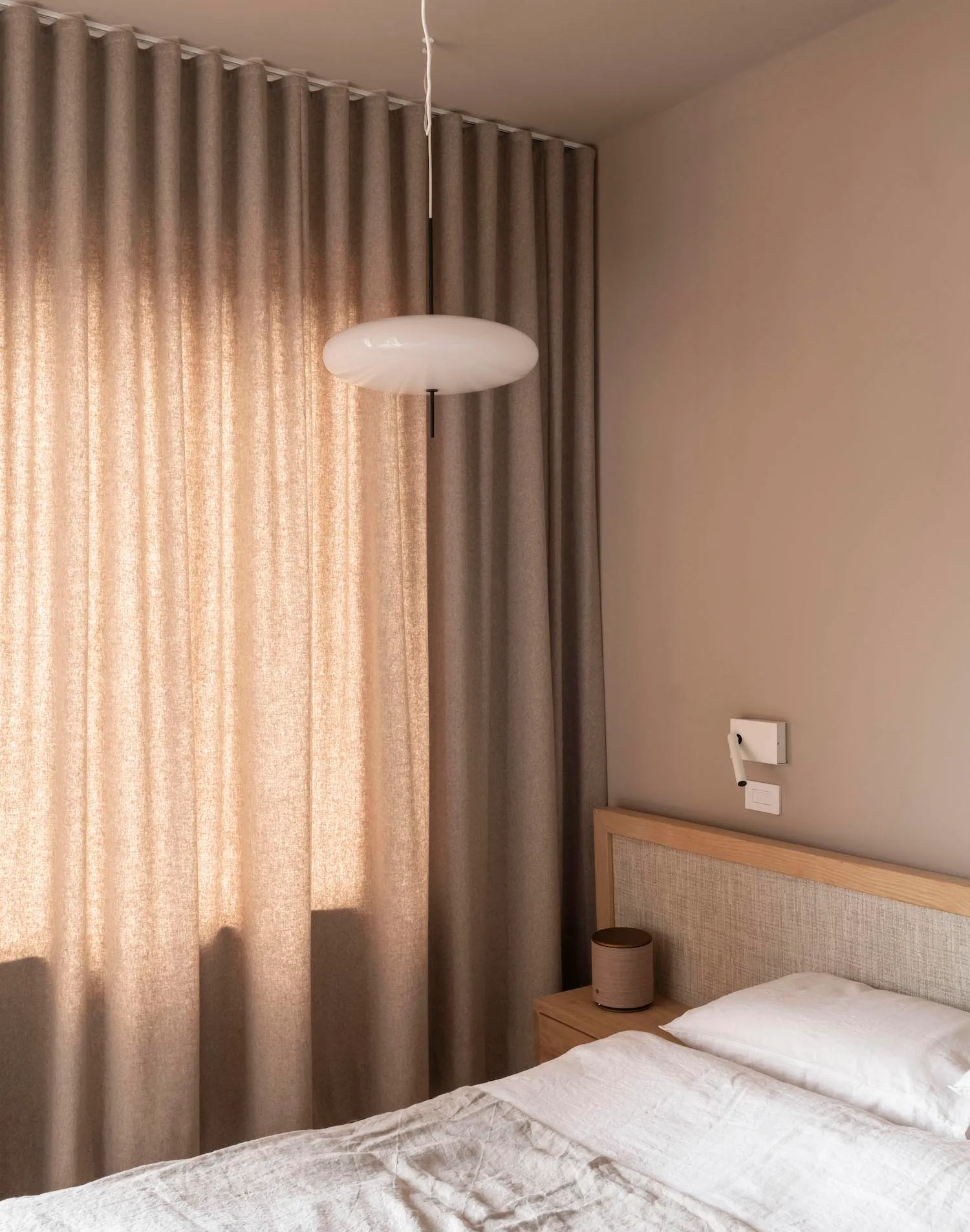 A minimalist bedroom with neutral textiles, wood accents, and a glass pendant light.