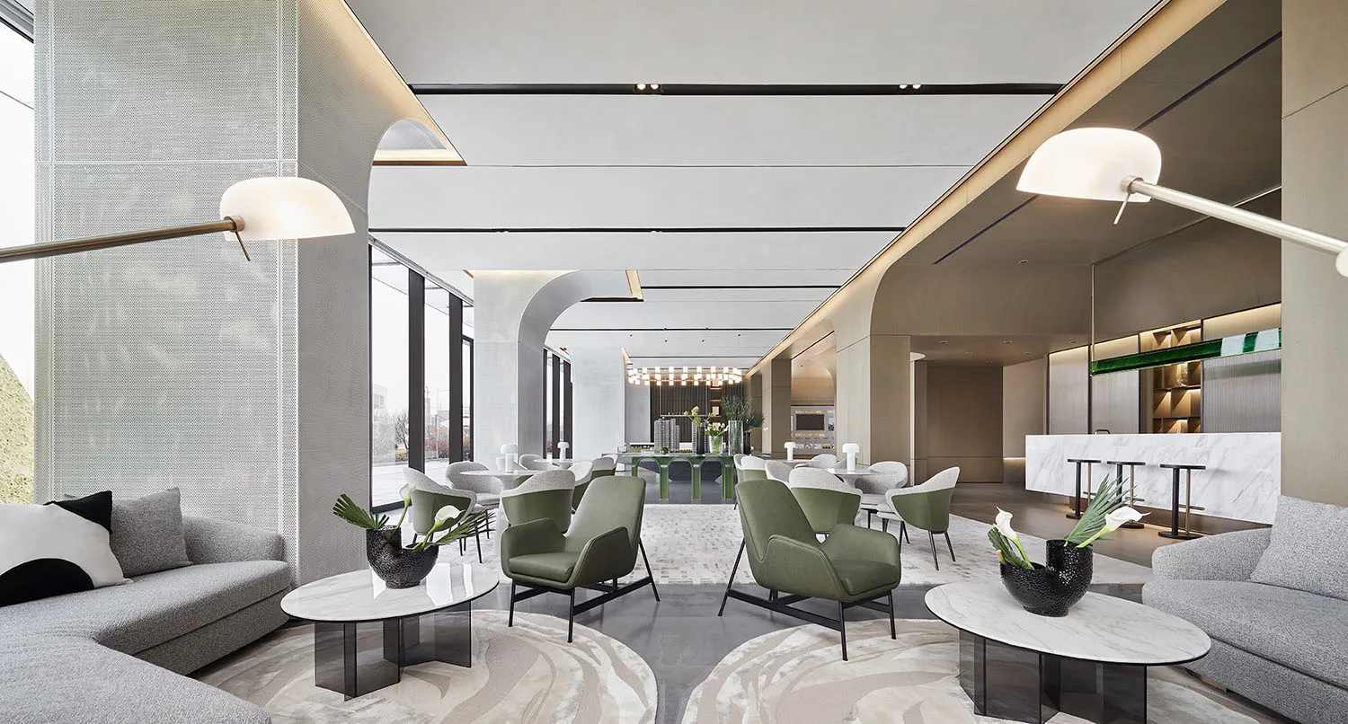 A modern lobby features gray sofas, green armchairs, white marble tables, and white lighting with organic furniture and concr