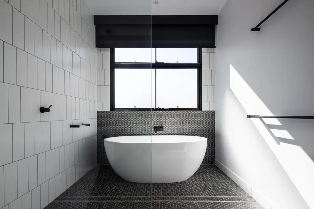 Modern minimalist bathroom with a freestanding bathtub, white tiled walls, and black textured walls and floor.