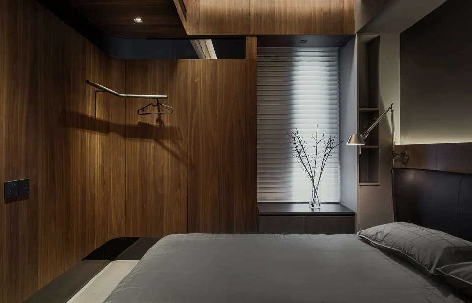 Modern minimalist bedroom featuring wooden-paneled walls and a neatly made bed with grey bedding.