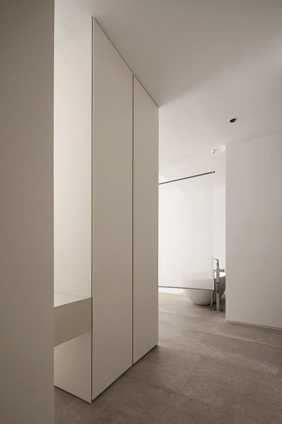 Modern minimalist bathroom with white walls and a concrete floor, featuring a freestanding bathtub and sleek, simple design.