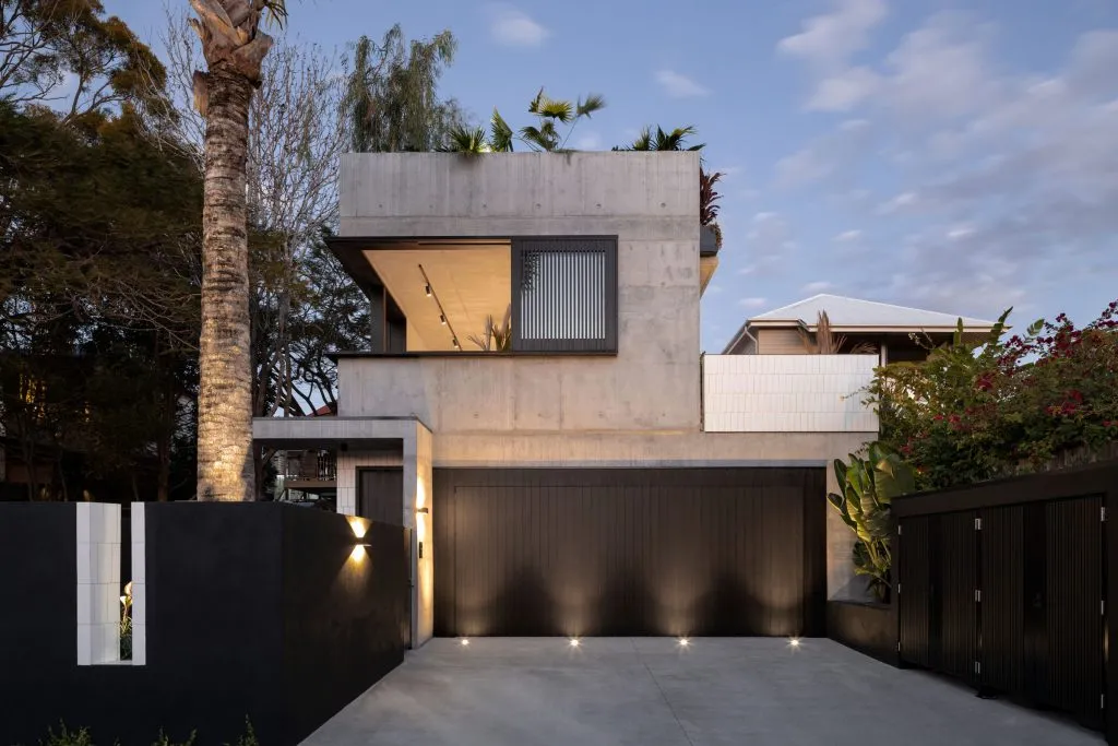 A modern concrete residence featuring a rooftop garden and black fence.