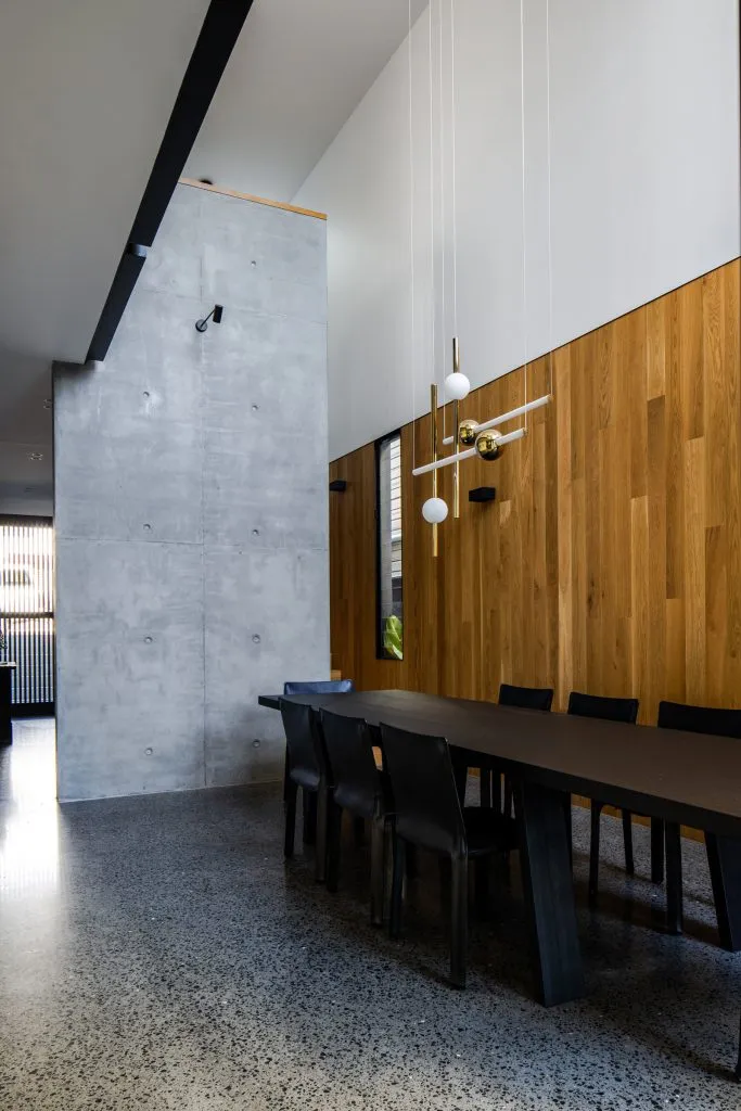 A modern dining room with concrete and wooden walls, black dining table and chairs, and contemporary white pendant lights.