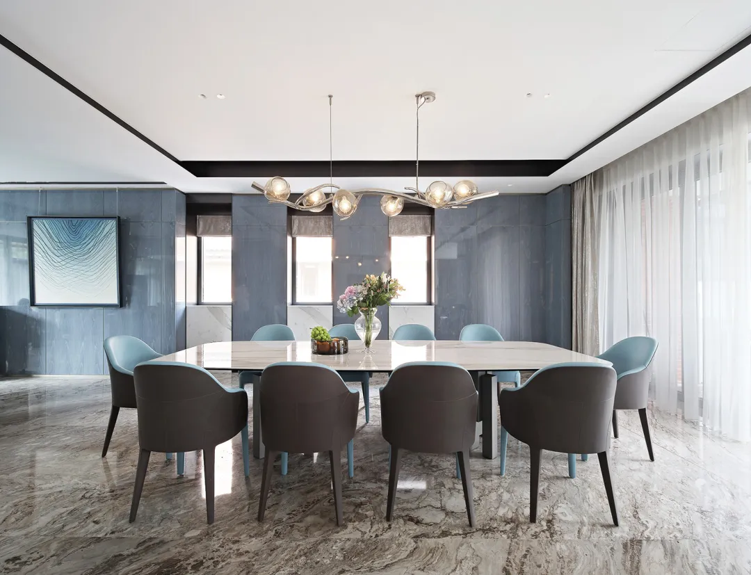 Modern dining room featuring a marble table and chairs, with a stylish chandelier and large windows.