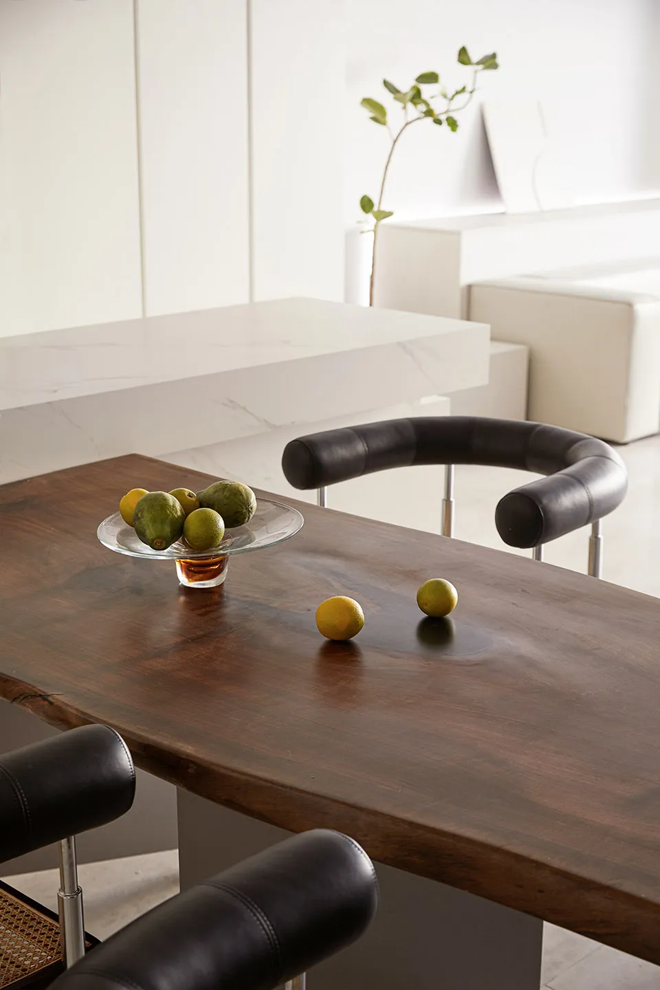 A modern dining space featuring a wooden table with a glass bowl of green and yellow fruits on it.