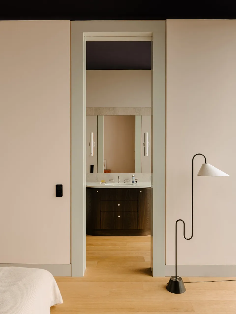 Modern minimalist bathroom interior with light wood flooring, beige and white walls, and a sleek white sink vanity.