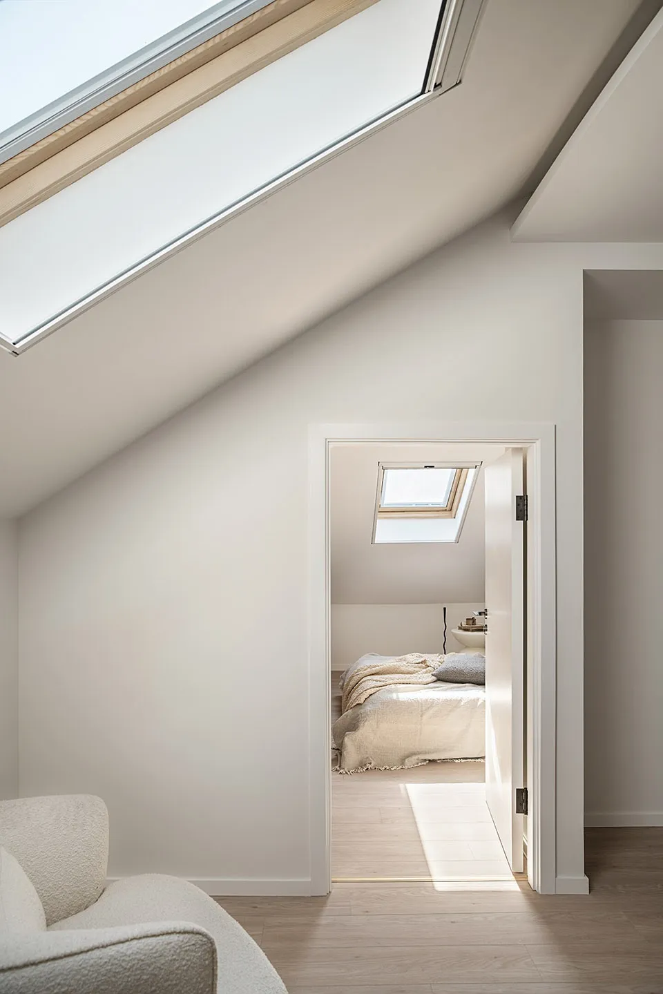 A minimalist bedroom featuring neutral-tones, white walls, and wooden elements with a skylight above, creating a serene and m