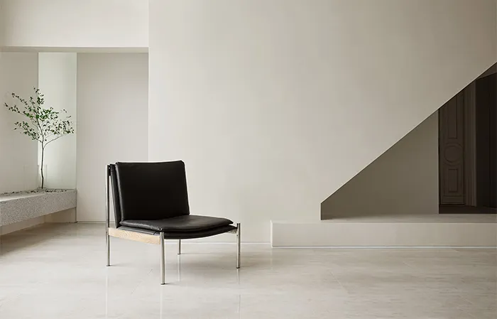 A minimalist interior with a black leather chair on a marble floor.