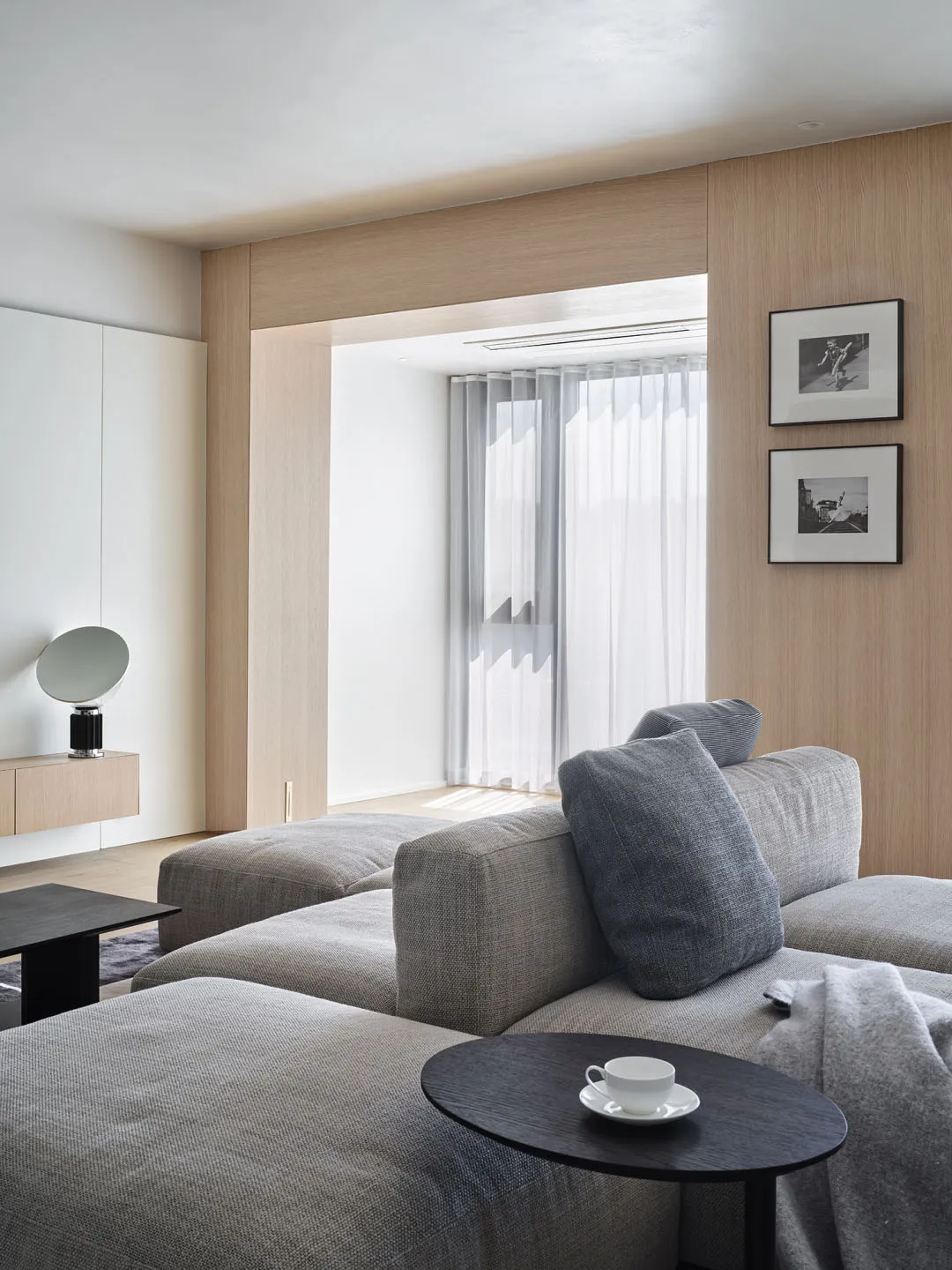 Contemporary living room with modern furniture, grey fabric sofa, black side table with cup and saucer, light wood paneling,