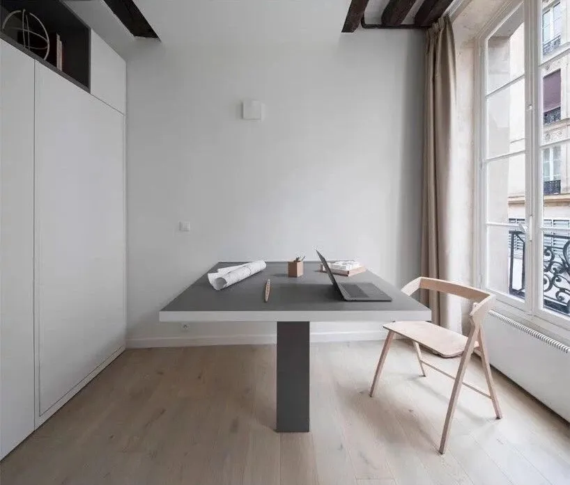 A minimalist office space featuring a modern concrete desk and wooden chair in front of a large window.