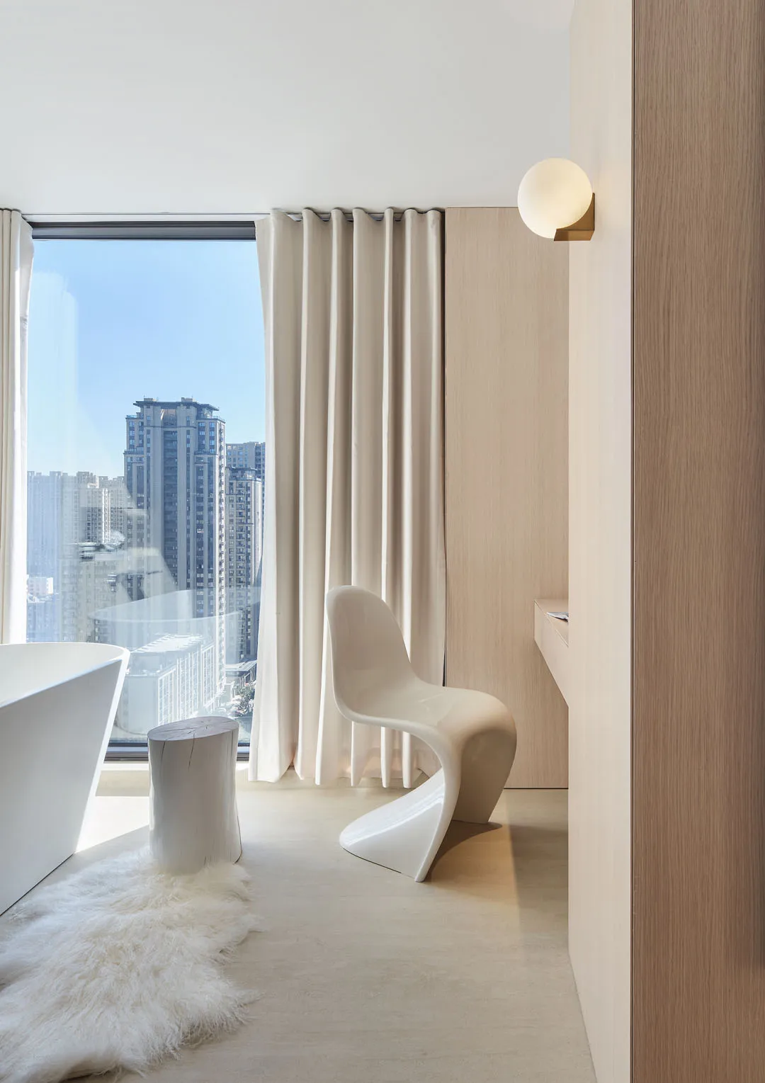 A modern minimalist bathroom with white decor, featuring a sleek white chair, a free-standing bathtub, a wooden stool, and a