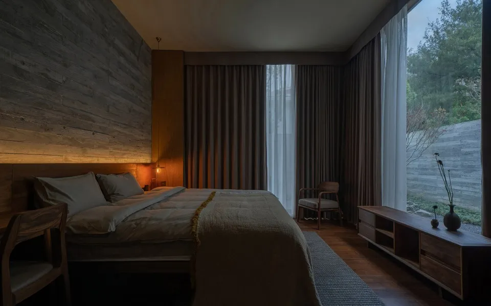 A minimalist bedroom featuring wooden elements and a large window with curtains.
