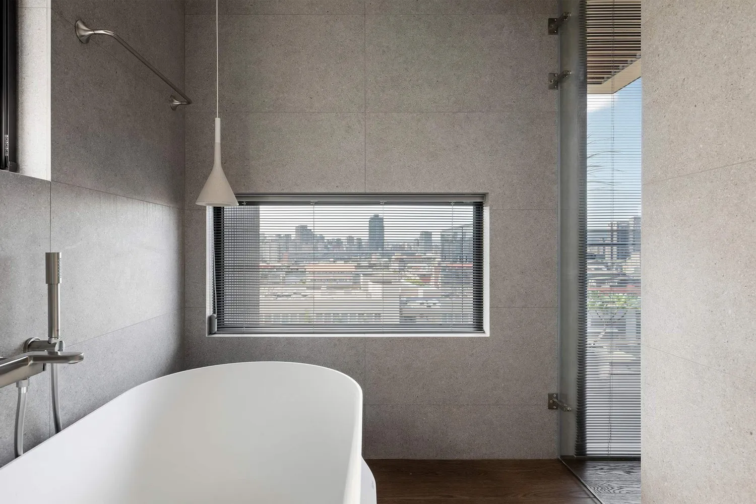 Modern bathroom with concrete tiles and blinds overlooking a city skyline.