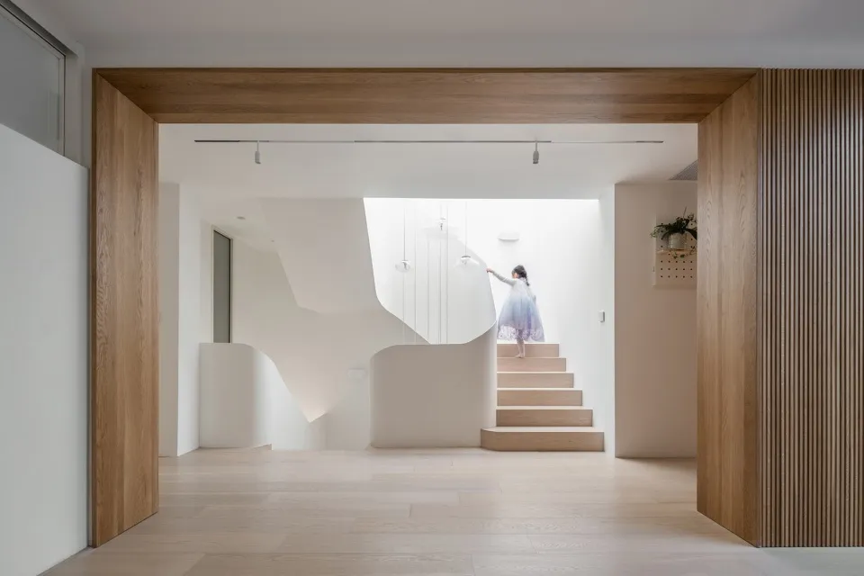 A modern family home staircase with wooden steps and a white concrete wall.