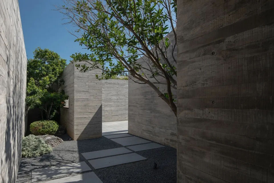 A modern landscape featuring concrete elements, surrounded by trees with shadows cast by the structure, set against a clear b