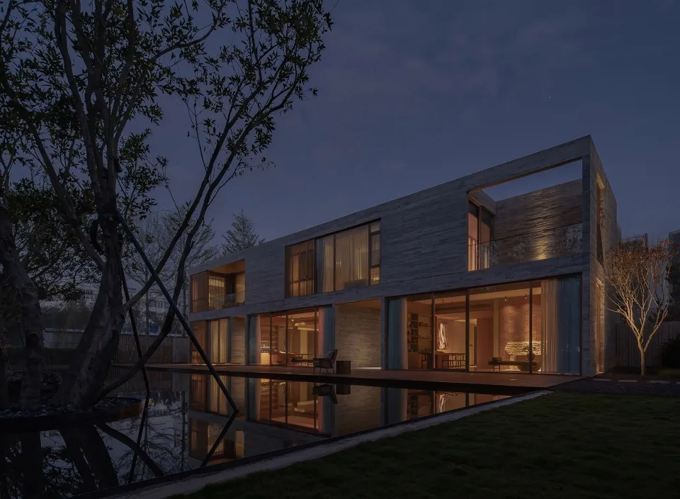 Modern minimalist house with wooden exterior at dusk, featuring large windows and a balcony.