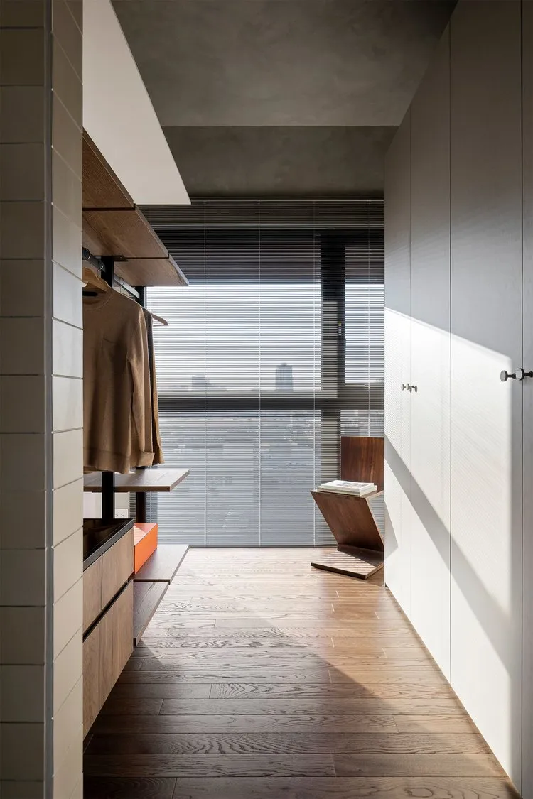 Minimalist modern closet with wooden flooring and fixtures, featuring a large window with blinds and a view of the city skyli