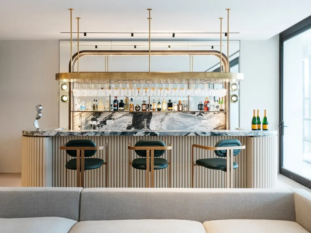 Modern interior bar featuring a marble counter with brass accents and upholstered seating.