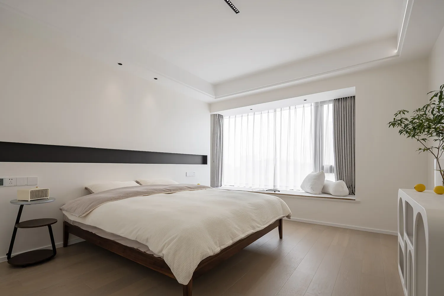 Modern minimalist bedroom with a queen-sized bed, white linens, and a large window with sheer curtains.