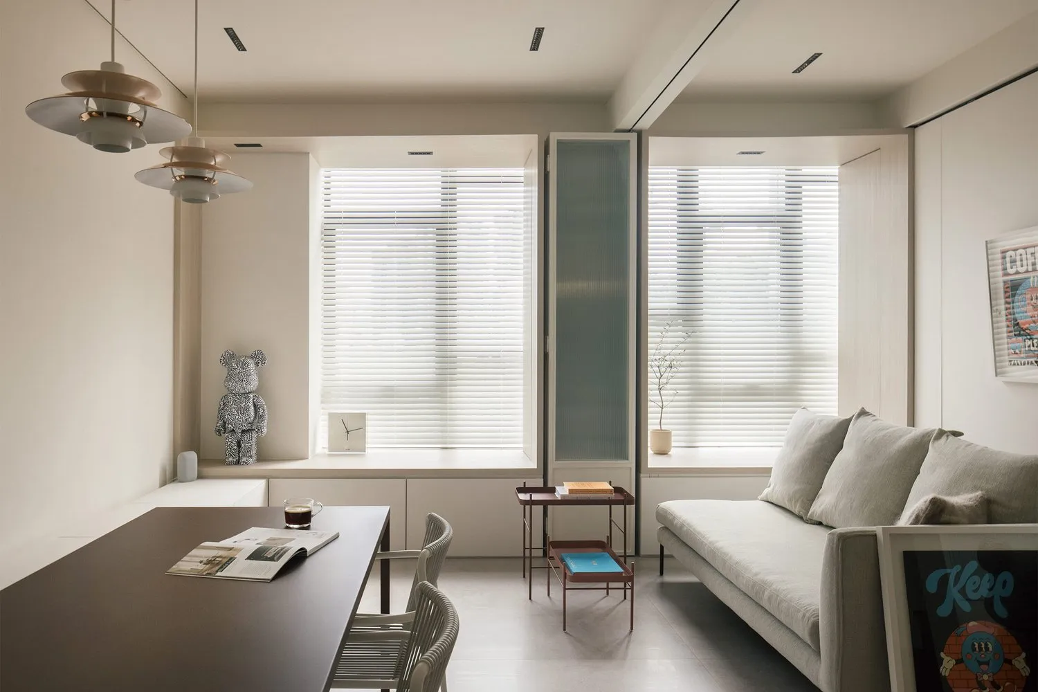 A modern minimalist living room with neutral colors, featuring a white sofa, a wooden coffee table, and a kitchen area with w