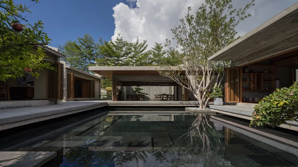 Modern residential pool with concrete walls and floors, surrounded by greenery, under a blue sky with clouds.