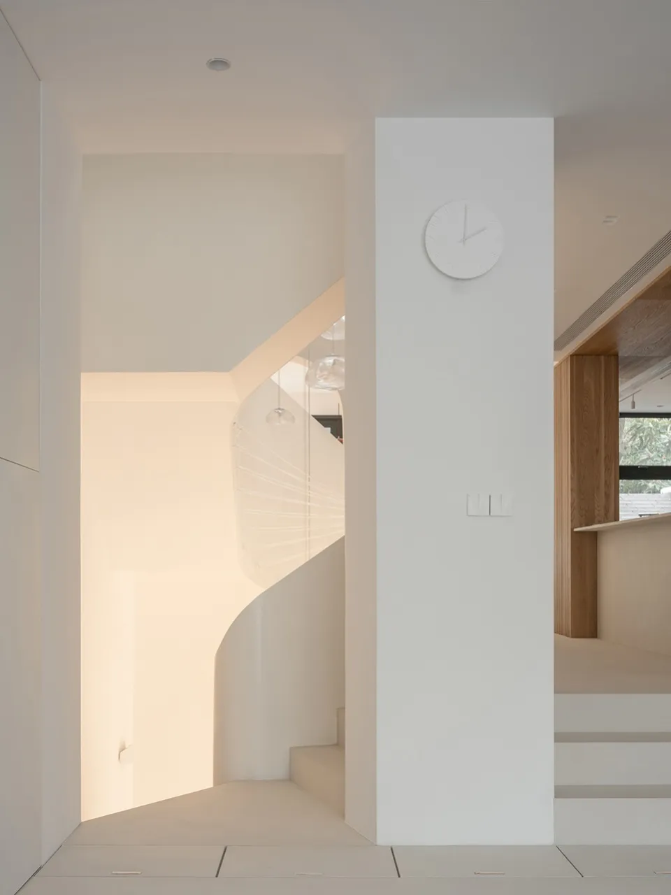 Modern white concrete staircase with minimalist design, featuring a wall clock and pendant lights.
