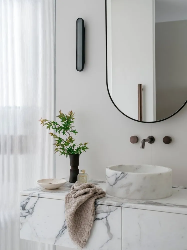 A minimalist bathroom featuring a marble counter with a vase, bowl, and towel hanging on it.
