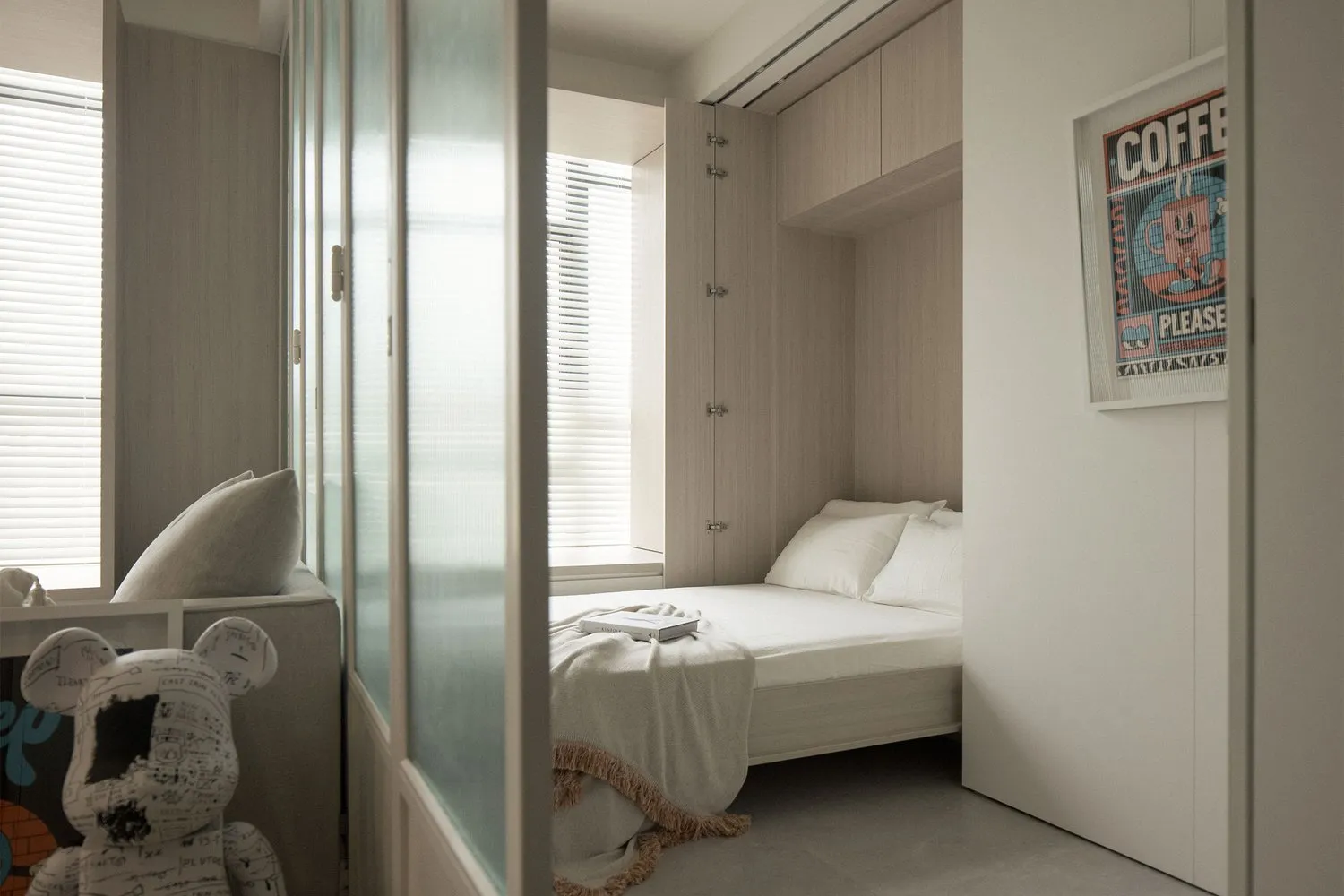 A minimalist bedroom with a wooden bed, white bedding, and textured fabric pillows.