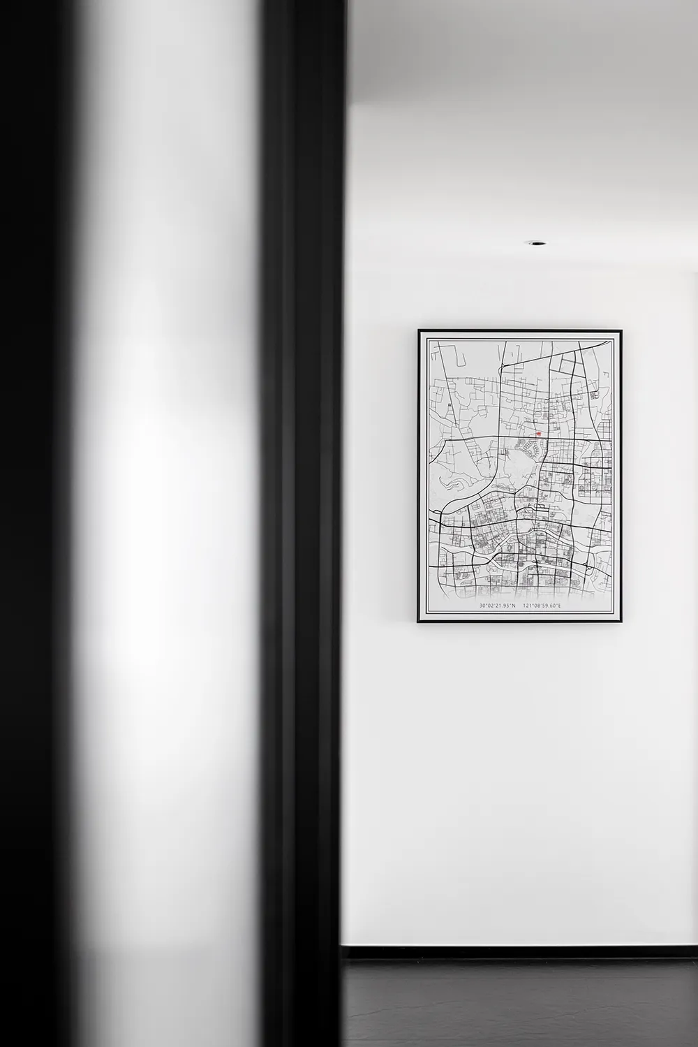 A minimalist black framed paper map on a white wall in a hallway.