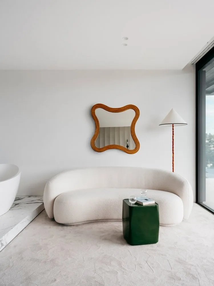Modern living room featuring a sleek, curved sofa upholstered in a light beige fabric, a white marble floor, and a green meta